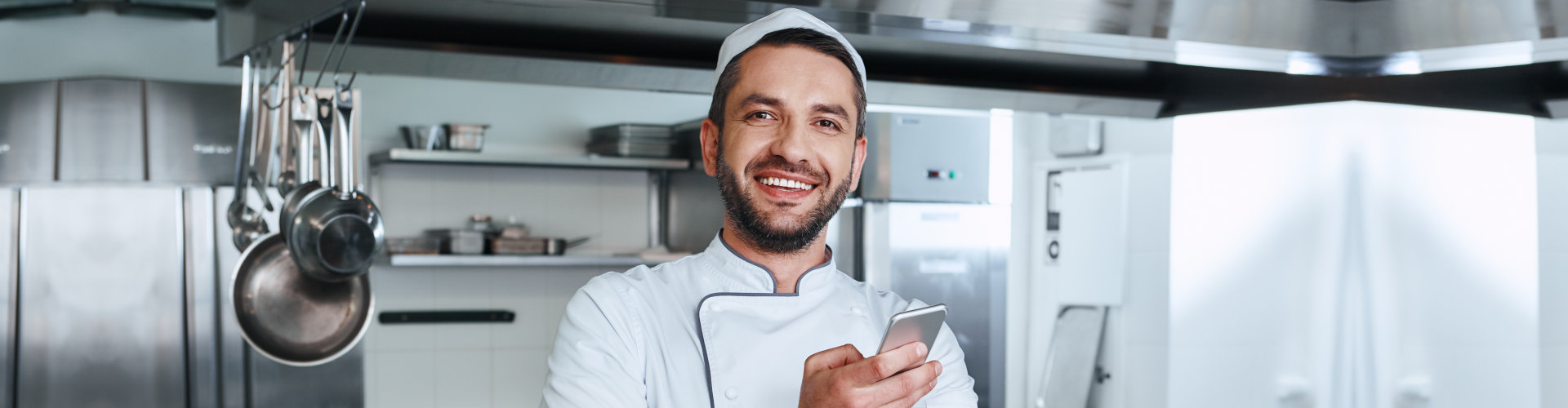 Happy cook standing in a kitchen while holding phone